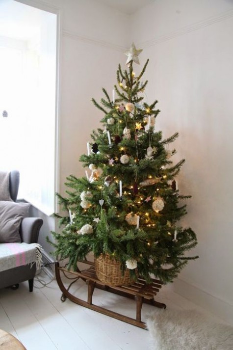 tree decorated with pompoms, pinecones and candles placed in a basket and on a sleigh