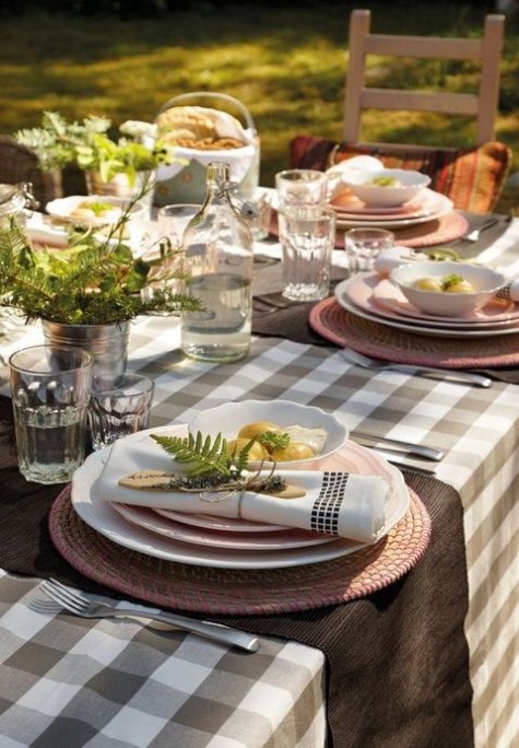 a checked tablecloth, a wicker platter and greenery in small buckets