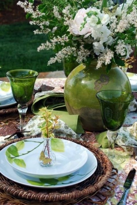 a tablescape with wicker chargers, green glasses, napkins and vases