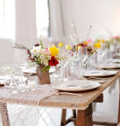 a wooden table with a macrame table runner, colorful flowers in pitchers