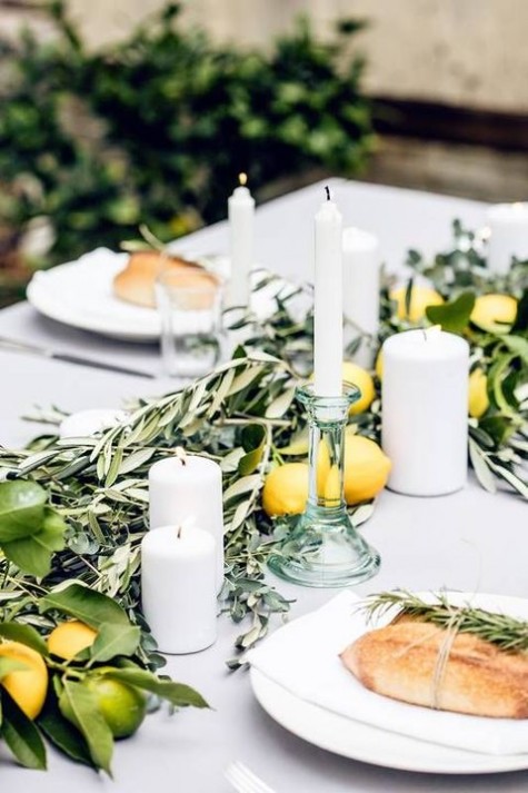 neutral table setting with glass candle holders, olive branches and citrus