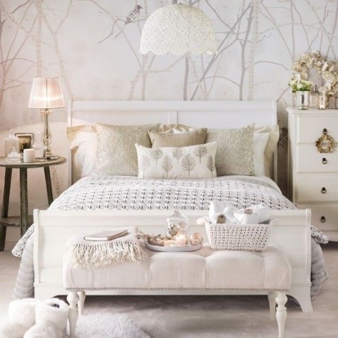 a creamy bedroom with an upholstered ottoman, a statament wallpaper wall and gold sequin pillows