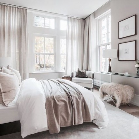 a glam feel is achieved with dusty pink curtains, pillows, a bedspread and a faux fur ottoman