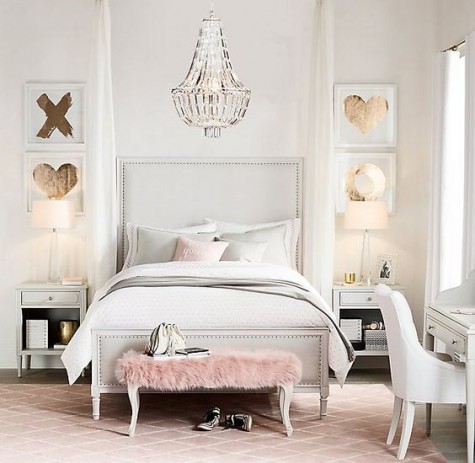 a gorgeous creamy bedroom with gold leaf artworks, a crystal chandelier, a faux fur ottoman and a pink rug