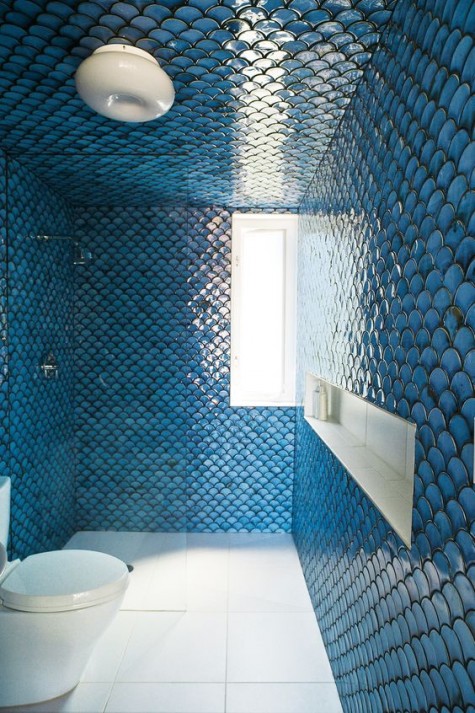 a small bathroom clad with blue fishscale tiles and the floor is contrasting white