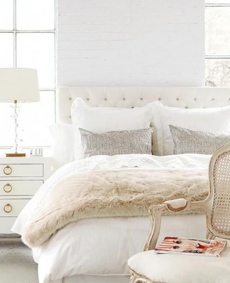a white and ivory bedroom with a faux fur bedspread, silver sequin pillows and a refined chair