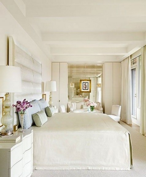 creamy bedroom with a large upholstered headboard, a mirror wall and a refined sofa