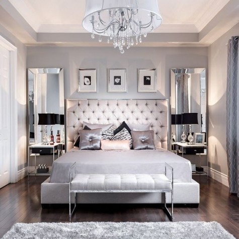 grey bedroom with a blush headboard, tall mirrors, a fluffy grey rug