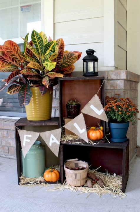 a crate display with a banner_ potted fall blooms_ pumpkins and hay