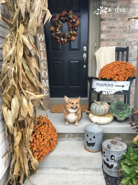 a rustic fall porch with corn husks_ a wreath_ putted mums and pumpkins