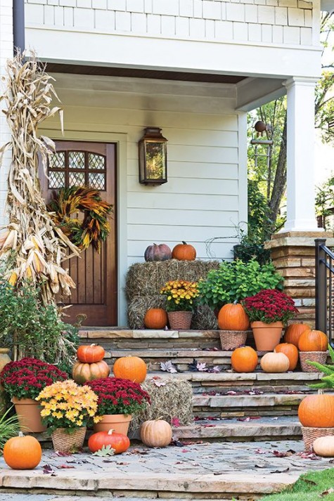 a rustic porch with hay_ lots of pumpkins_ corn and corn husks and potted flowers