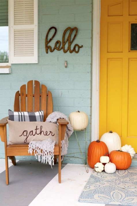 simple porch decor with a wooden chair_ white and orange pumpkins_ pillows and a blanket