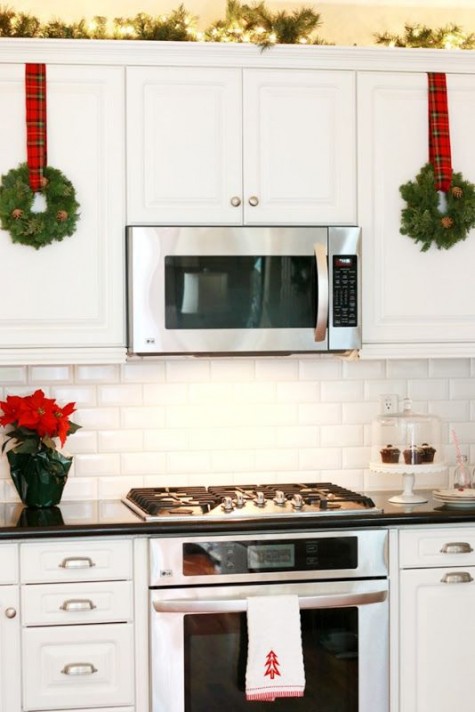 an evergreen wreath with pinecones and plaid ribbon on the cabinets