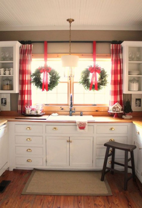 wreaths with red ribbon hanging on the window and plaid curtains