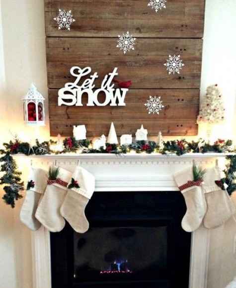 a pallet sign with snowflakes, an evergreen garland with stockings and a lantern with ornaments