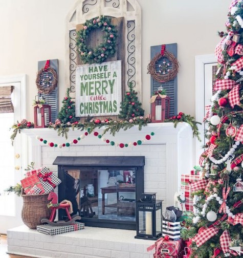 red, green and white mantel with a pompom garland, lanterns, wreaths, trees and a sign