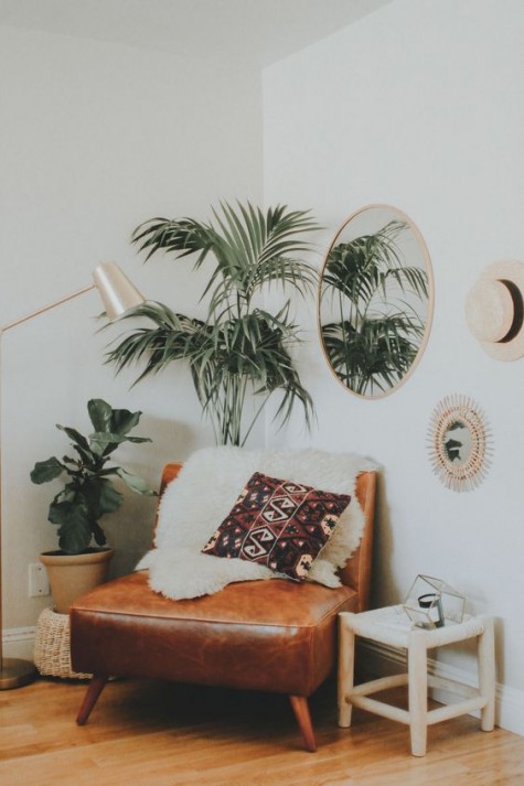 a boho chic reading nook with a leather chair, a stool, some greenery and a lamp