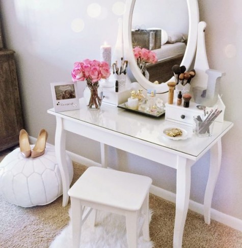 a glass top vanity, a comfy mirror, a stool and a white leather ottoman for creating a girlish feel