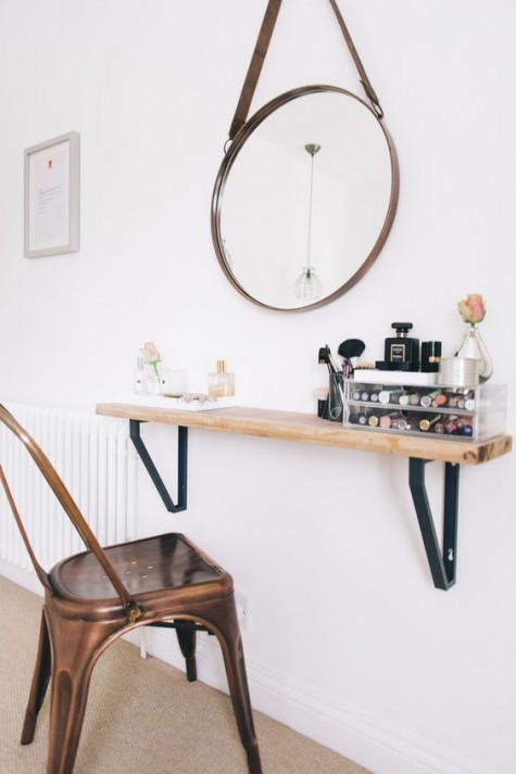 a mini makeup nook with a narrow wooden shelf, a round mirror and comfy storage