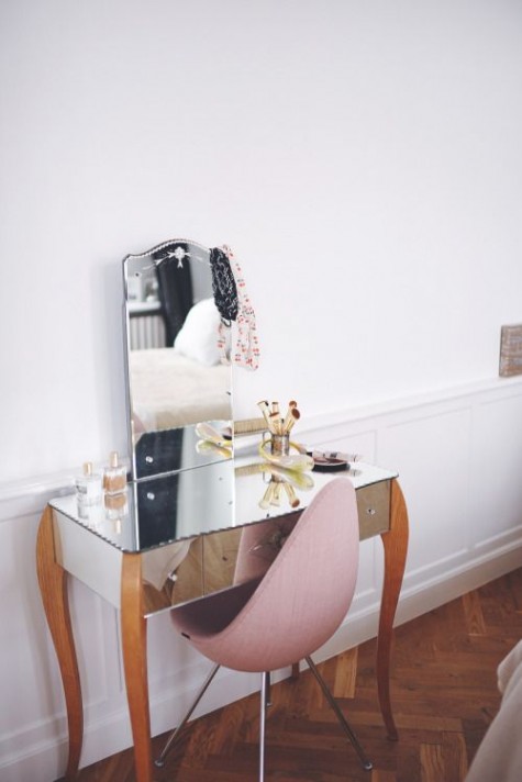 a unique mirrored vanity with wooden legs and a pink egg-shaped chair
