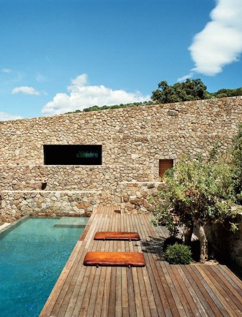 a Mediterranean-style deck with trees, a stone wall and a long and narrow pool
