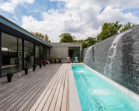 a backyard with a deck and a long and narrow pool with waterfalls