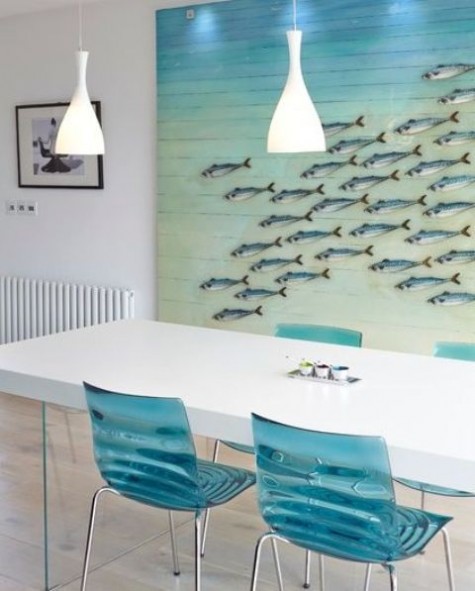 a beach-inspired dining room with an oversized fish artwork and clear blue chairs