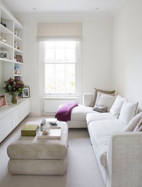 a tiny living room with a corner sofa, a large ottoman and a shelving unit