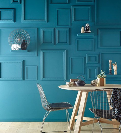 a dining space with a teal wall and matching empty frames