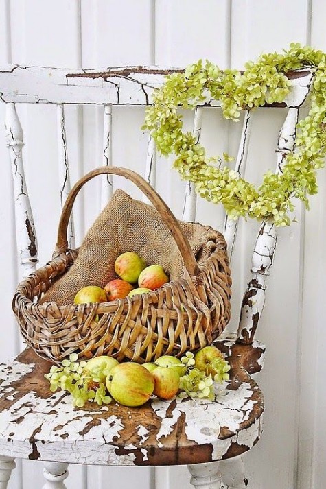 a harvest themed fall display with a greenery wreath and a basket with burlap and apples