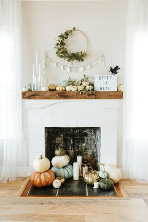 a modern pumpkin display on the mantel and next to the fireplace plus greenery and candles