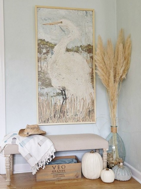 a neutral fall entryway with wheat, pumpkins and a checked blanket